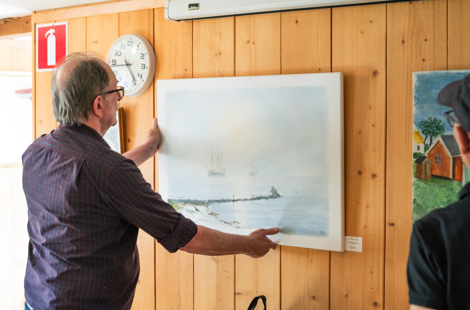 Ingvar ”Jison” Stendahl hänger upp en av sina målningar, en disig marin med segelfartyg, i galleriet på Skomakaregården.